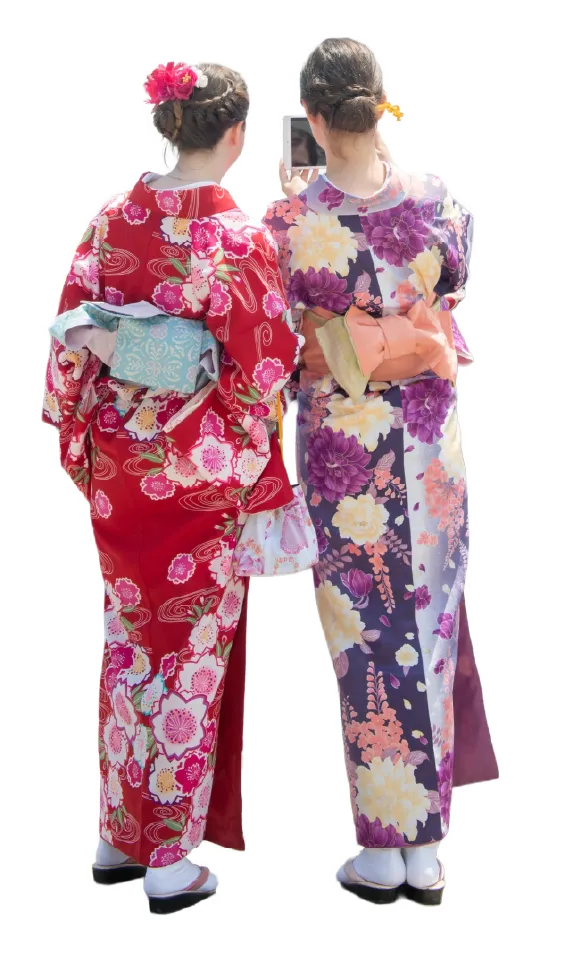 Rear view of two women in traditional Japanese kimono — one in red floral and one in purple floral pattern — wearing flower hair accessories and wooden geta sandals, standing side by side